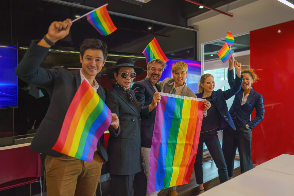 A photograph of colleagues in a workplace, celebrating pride and holding rainbow flags.