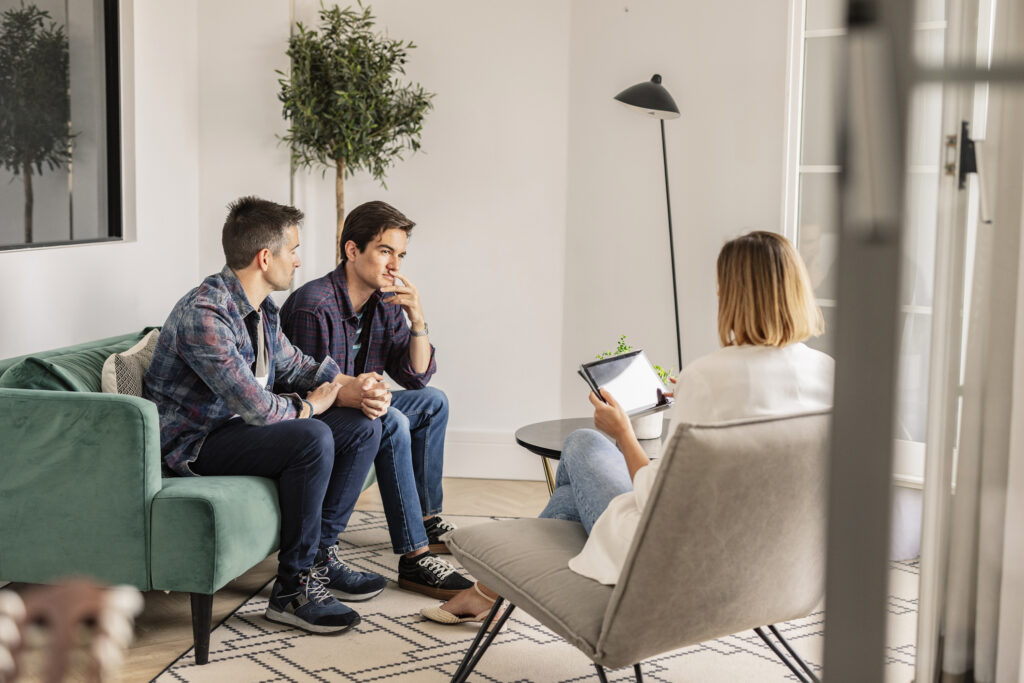 A photograph of two gay men in therapy, discussing the affects of conversion therapy on their mental health.